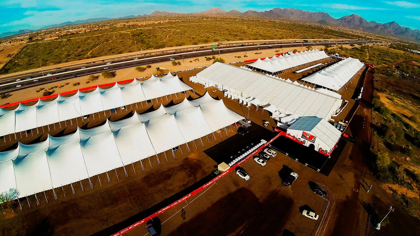 Aerial view of a large complex of white peaked tents arranged in rows across a paved site.
